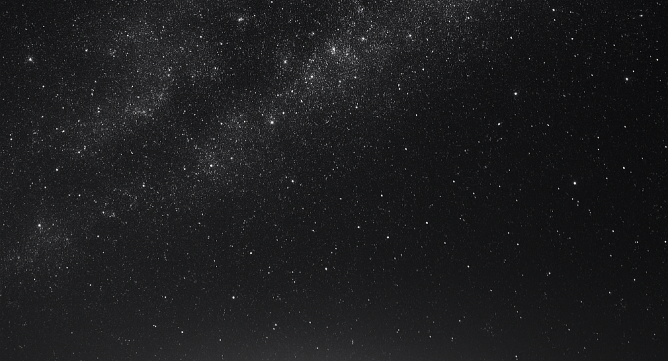 A group of men and women stand on a shore, looking up at a vast, detailed starry sky over dark water, emphasizing existential scale.